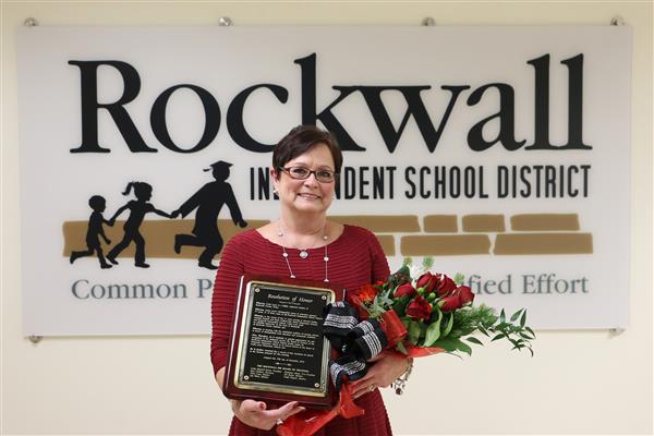 Linda Lyon standing infront of Rockwall ISD sign with flowers.